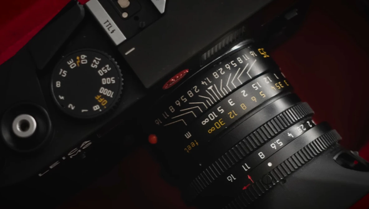 Overhead view of a rangefinder film camera with manual focus lens on dark surface with red fabric.