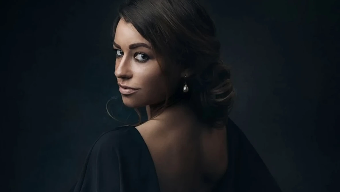 Woman with dark hair looking over shoulder against dark background.