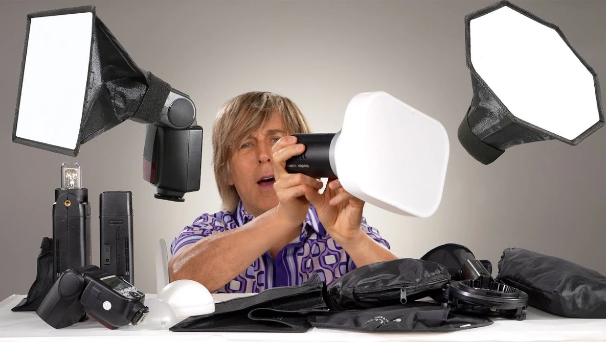 Photographer examines camera flash and softbox diffuser among studio lighting equipment.