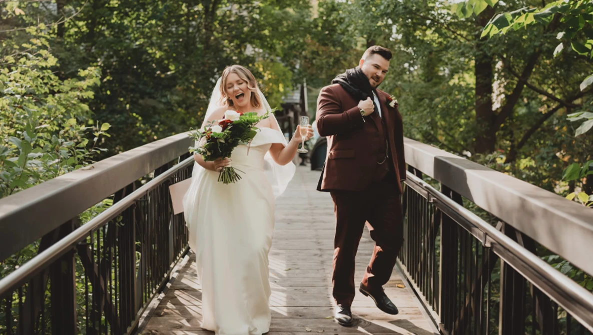 Bride and groom walking together on a wooden boardwalk surrounded by green forest canopy.