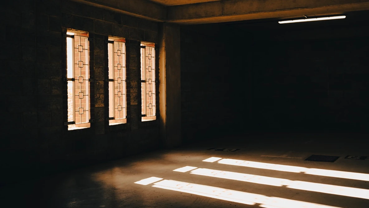 Sunlight streaming through three narrow windows into a dark interior space, creating geometric shadows on the floor.