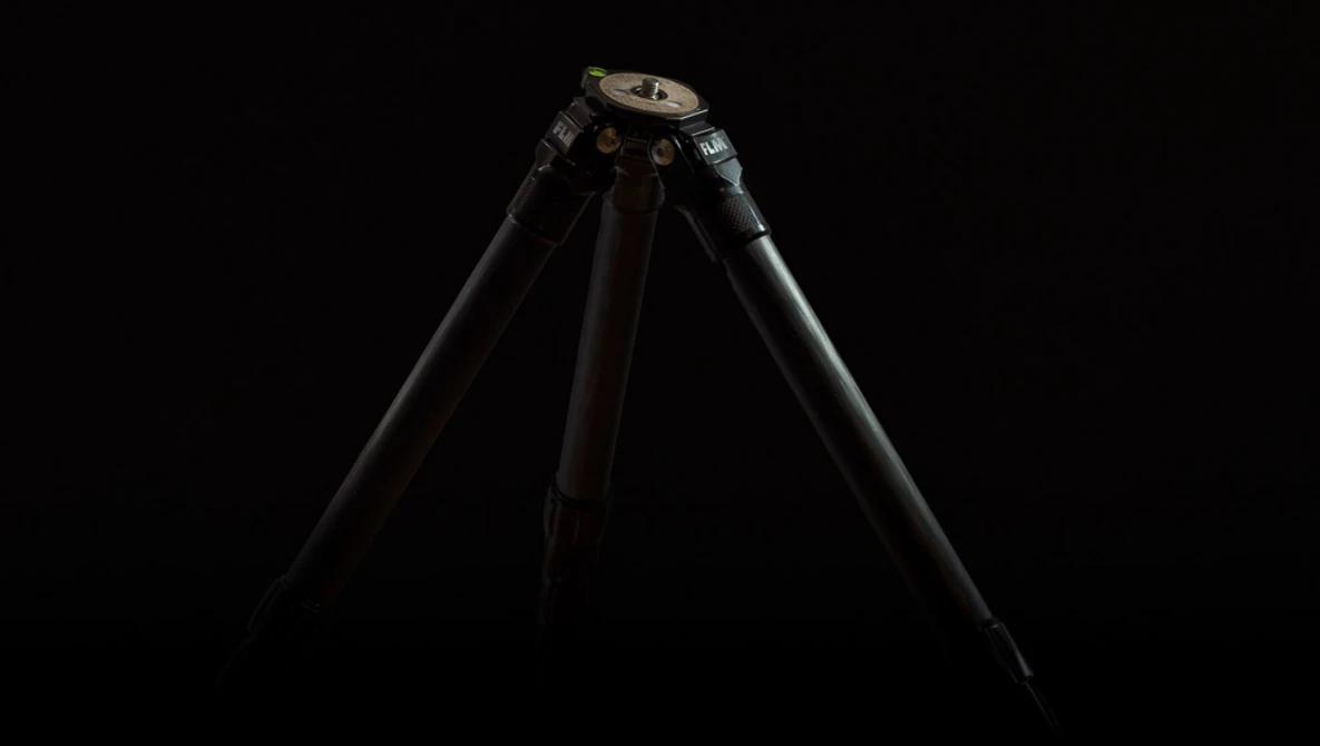Professional tripod with black legs and metal head against dark background.