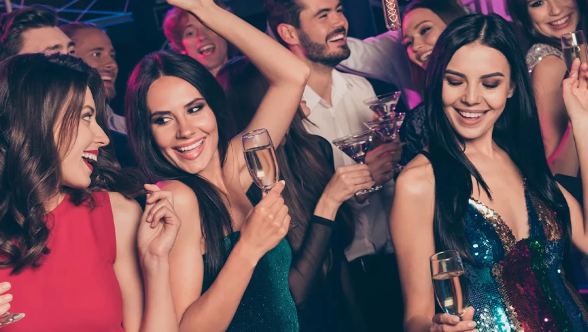 Group of people in formal attire celebrating with champagne glasses at a nightclub or party venue.