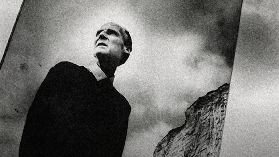 Man in dark clothing gazing upward against dramatic cloudy sky in high-contrast black and white photography.