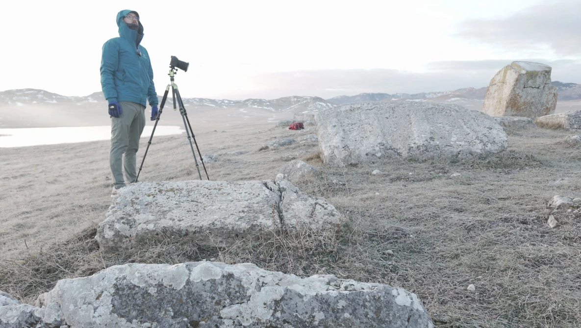 Photographer with tripod-mounted camera documenting rocky terrain in arid landscape.