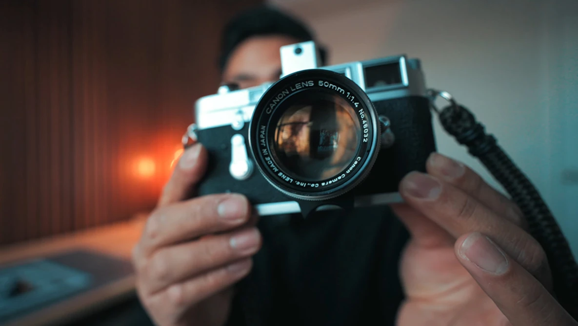 Photographer holding a vintage rangefinder camera with a wide-aperture lens pointed toward the camera.