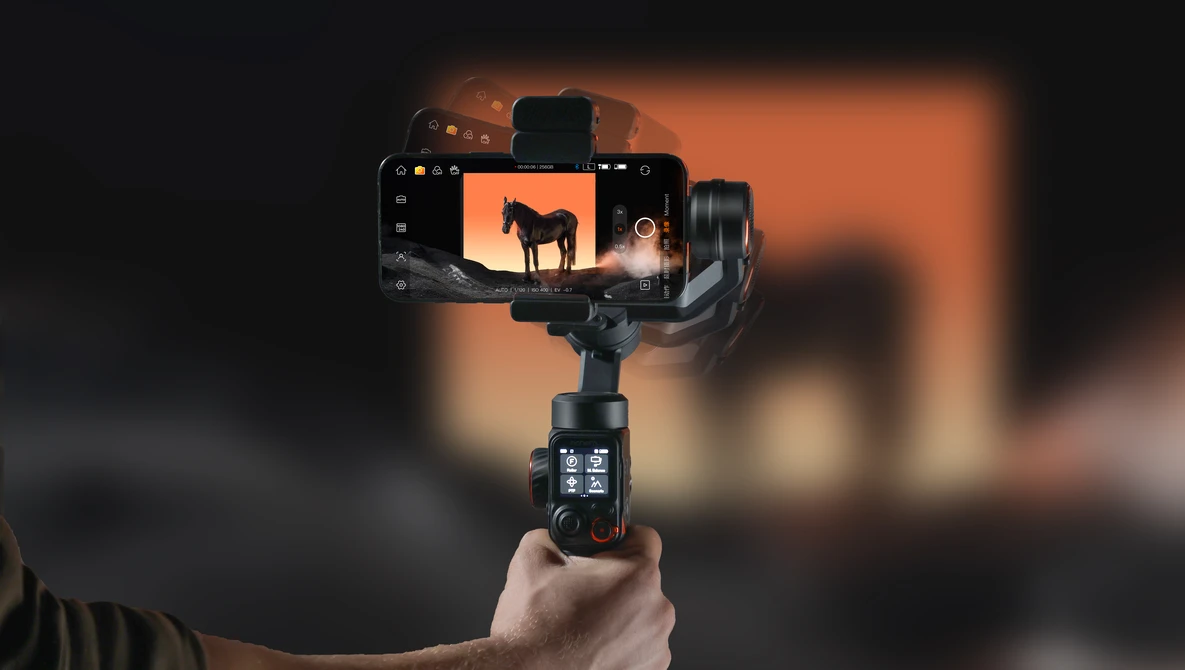 Hand holding a smartphone gimbal stabilizer with mounted phone displaying sunset silhouette footage.