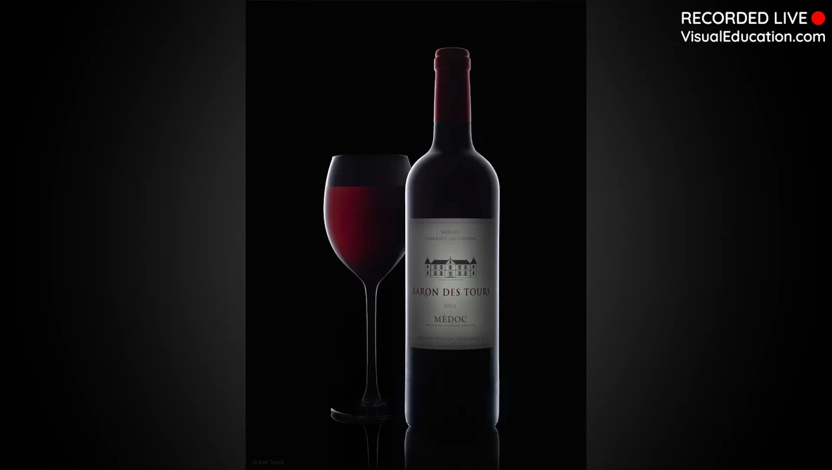 Wine bottle and filled glass against a black background with dramatic side lighting.