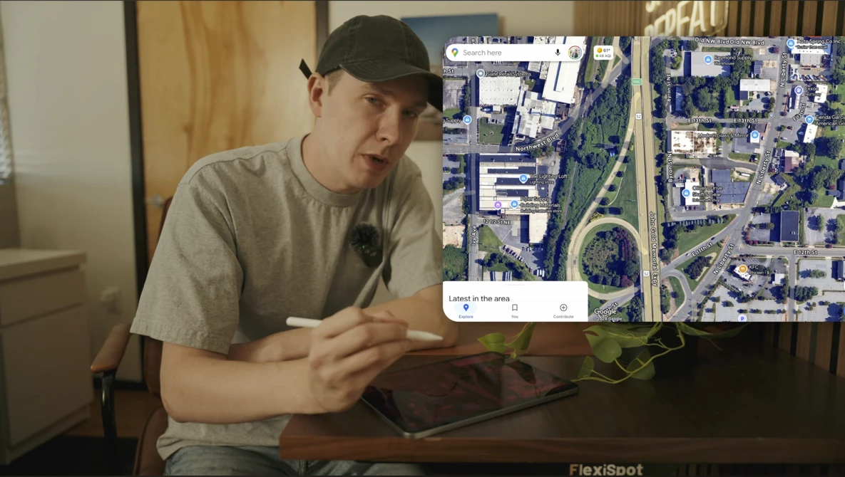 Person gesturing toward aerial satellite map displayed on tablet screen.