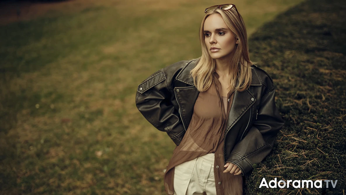 Woman in black leather jacket and neutral tones standing in overgrown field during golden hour.