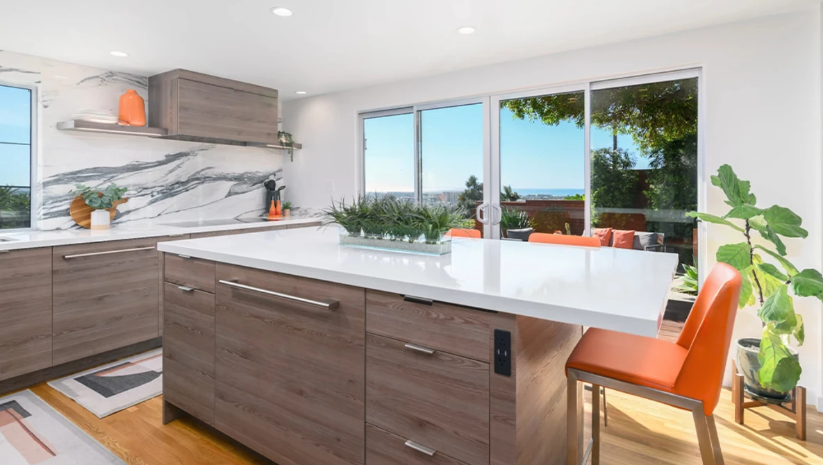 Modern kitchen with gray wood cabinetry, white quartz countertop, and large windows overlooking a landscape.