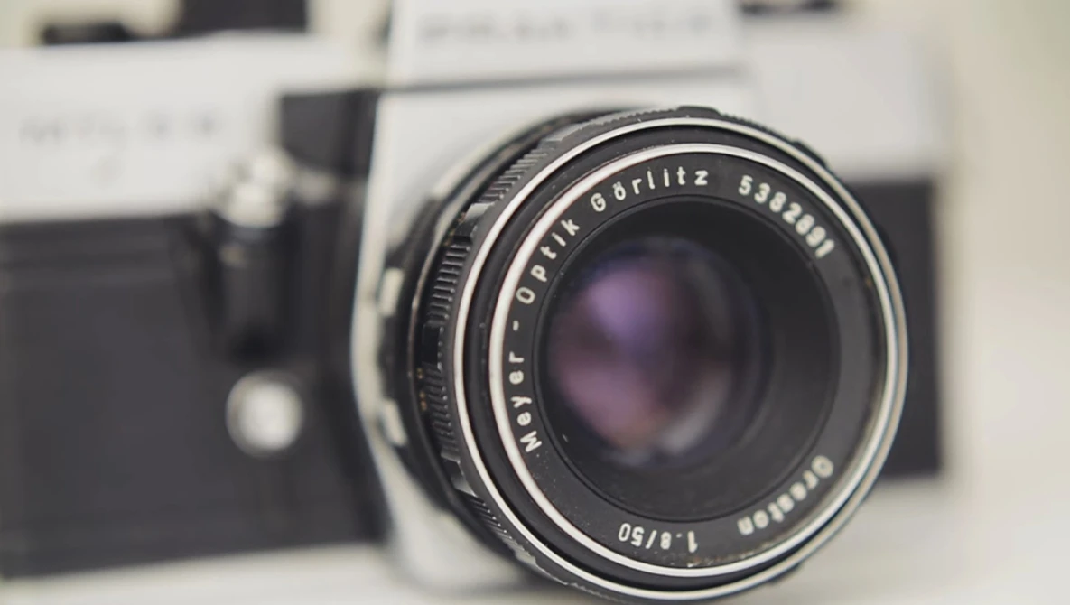 Vintage rangefinder camera with fast prime lens in sharp focus, blurred film camera body visible in background.