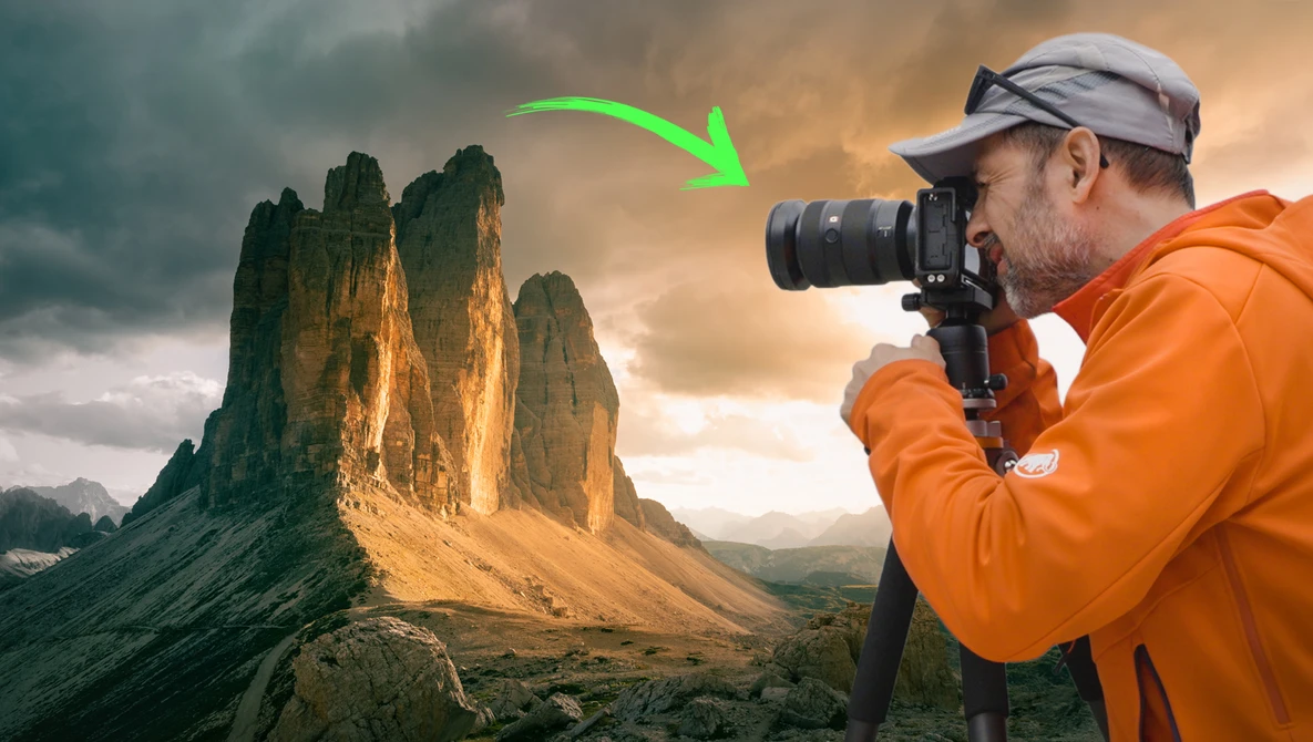 Photographer in orange jacket photographing dramatic mountain peaks during golden hour.