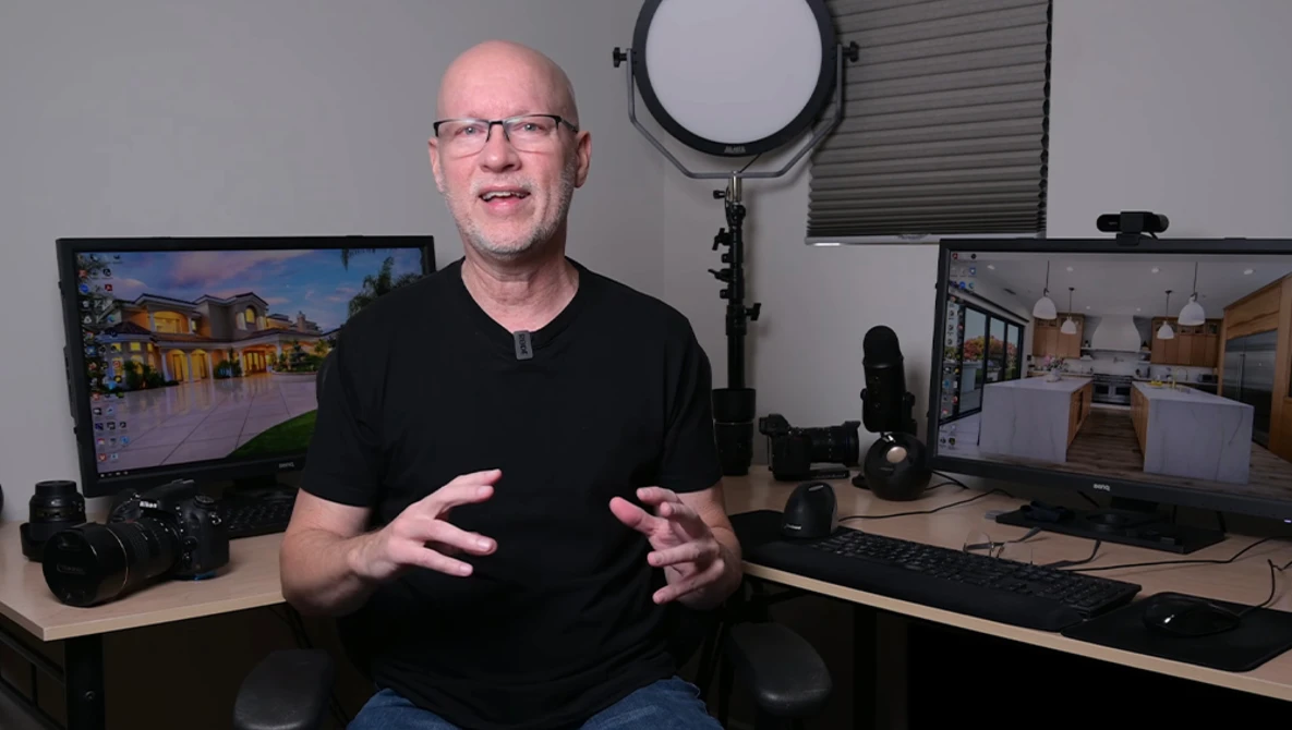 Bald man with glasses speaking to camera in a photography studio setup with dual monitors and professional lighting equipment.