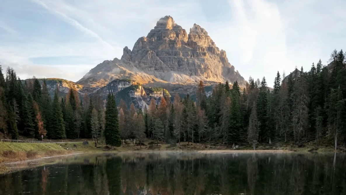 Jagged mountain peak reflected in still lake surrounded by coniferous forest.