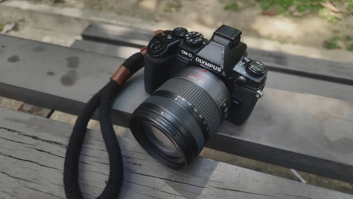 Olympus mirrorless camera with attached zoom lens and black camera strap on wooden surface.