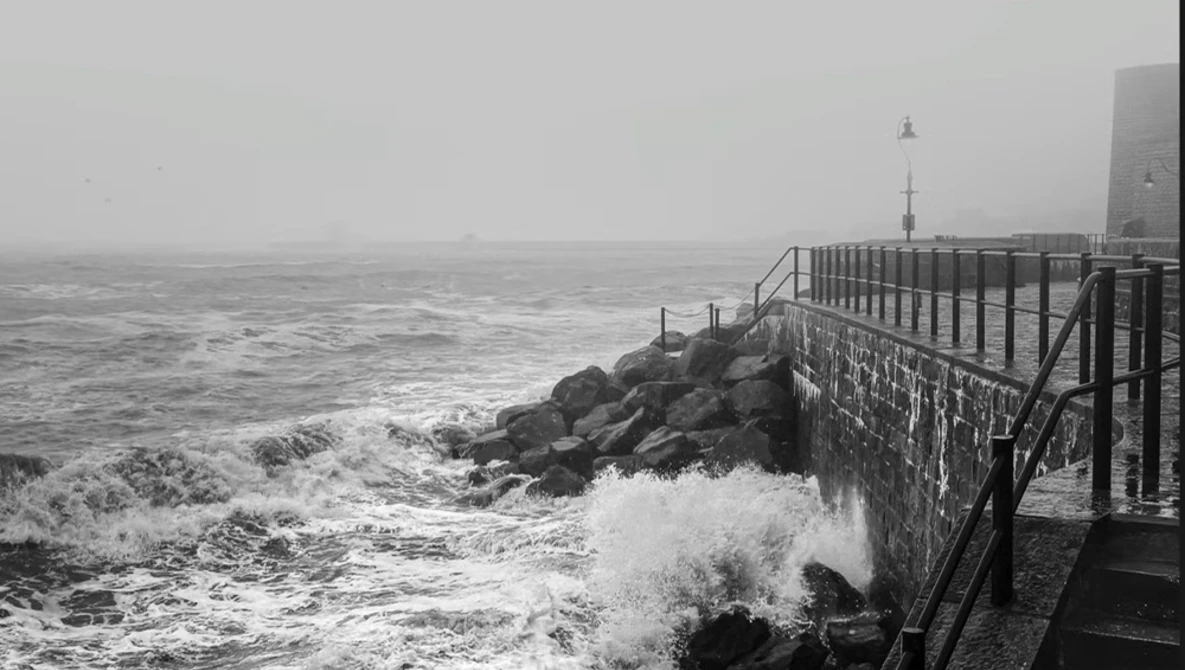 Dramatic seascape with crashing waves against a concrete seawall and rocky breakwater in stormy weather.