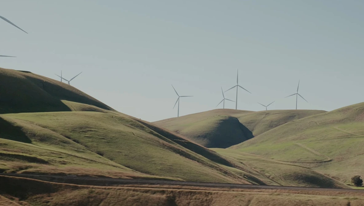 Rolling hills with wind turbines on distant ridge under overcast sky.