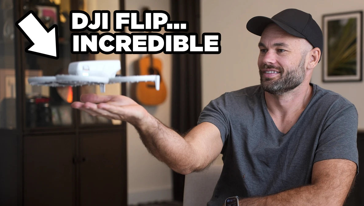 Man holding a small drone while gesturing toward it in an indoor setting.