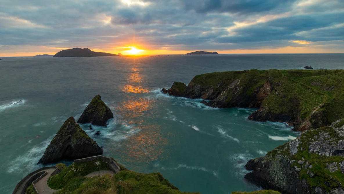 Dramatic sunset over dramatic coastal cliffs with turquoise waters and distant islands on the horizon.