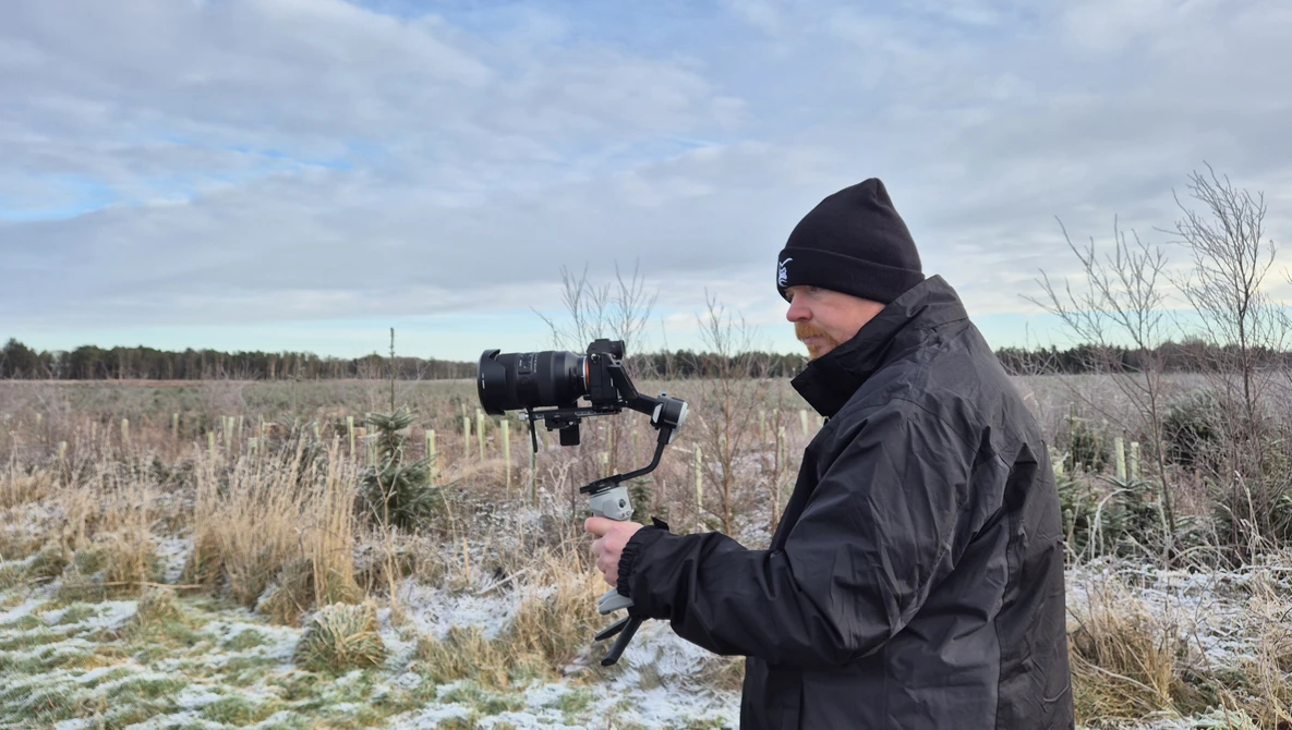 Videographer operating a camera mounted on a gimbal stabilizer in a snowy field.