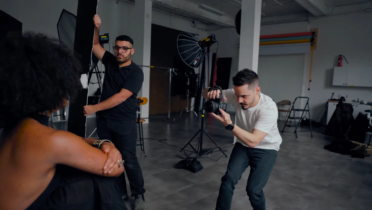 Photography crew adjusting lighting equipment during a studio shoot with a model in foreground.