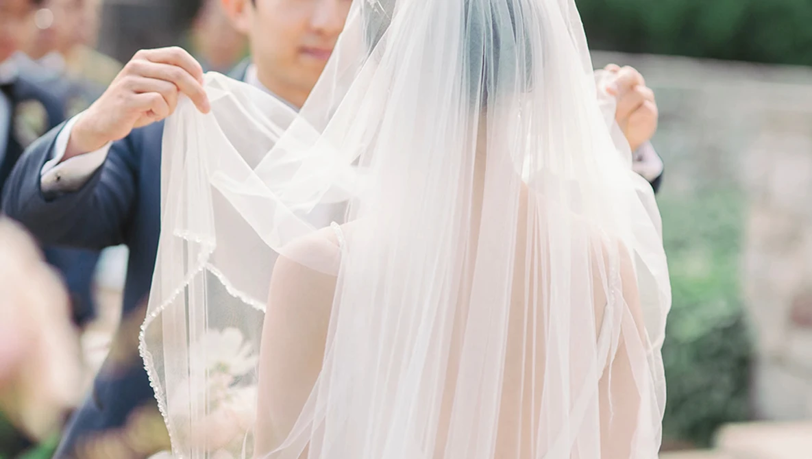 Groom adjusting bride's flowing veil during wedding ceremony.