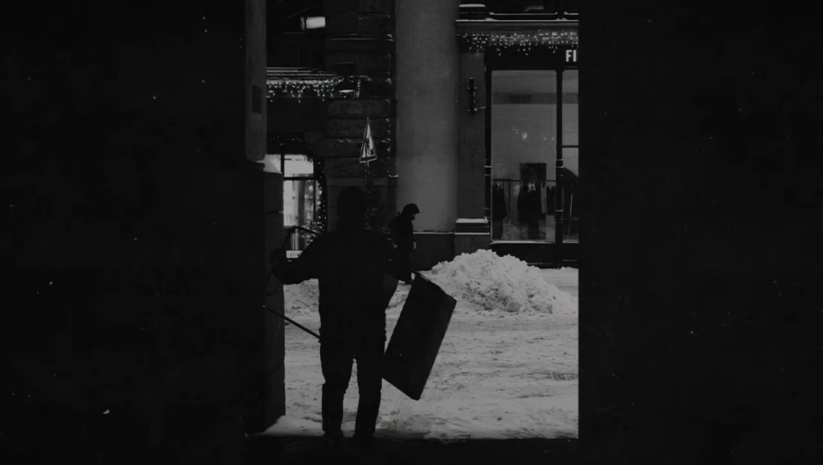 Silhouetted figure in dark coat holding briefcase, framed by building entrance in snowy urban setting.