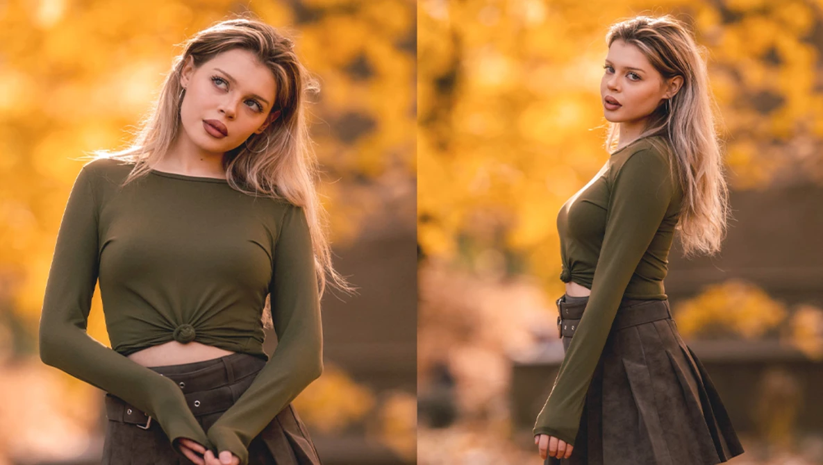 Woman in olive long-sleeve crop top and dark skirt posed against warm golden autumn foliage background.