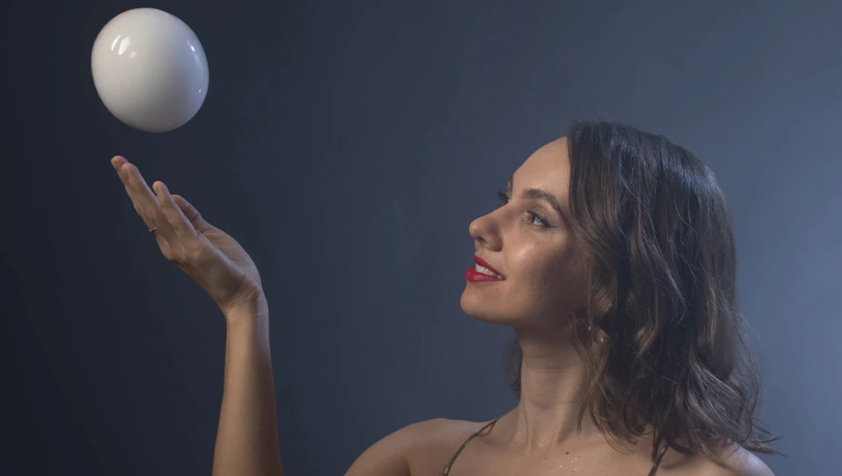 Woman in profile tosses a white sphere upward against a dark blue background.