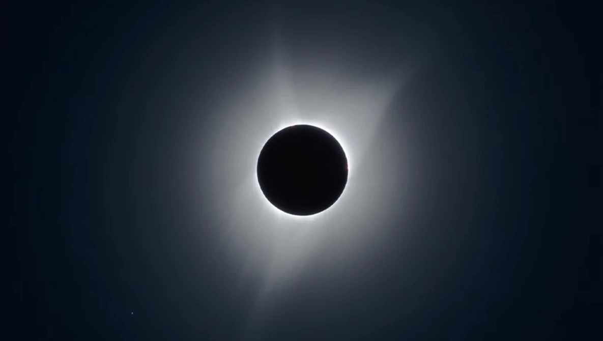 Total solar eclipse with moon silhouette centered against bright corona and darkened sky.