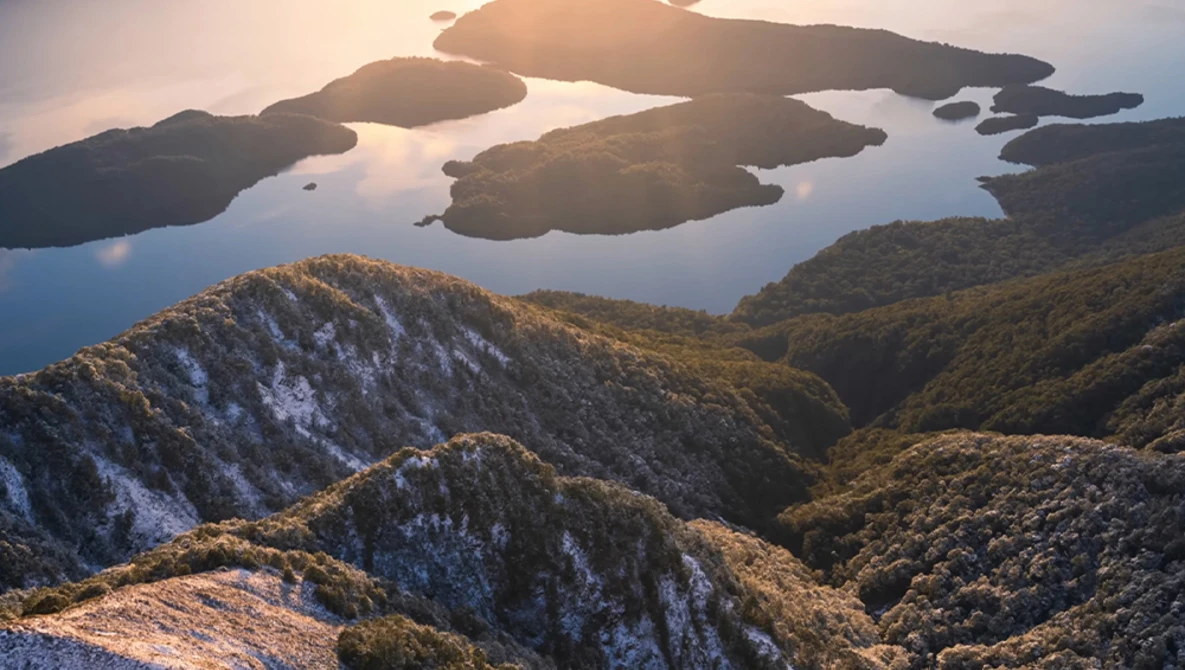 Forested mountains and islands at golden hour with still water reflecting the sky.