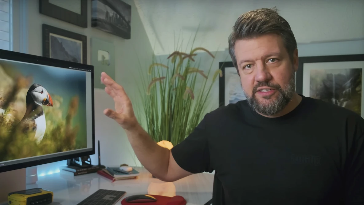 Man gesturing toward monitor displaying puffin photograph in studio setting.