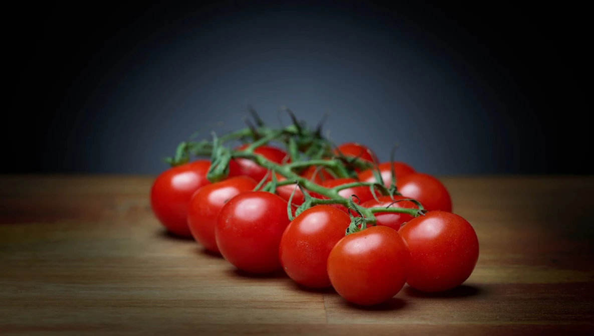 Cluster of ripe tomatoes with green stems on wooden surface against dark background.