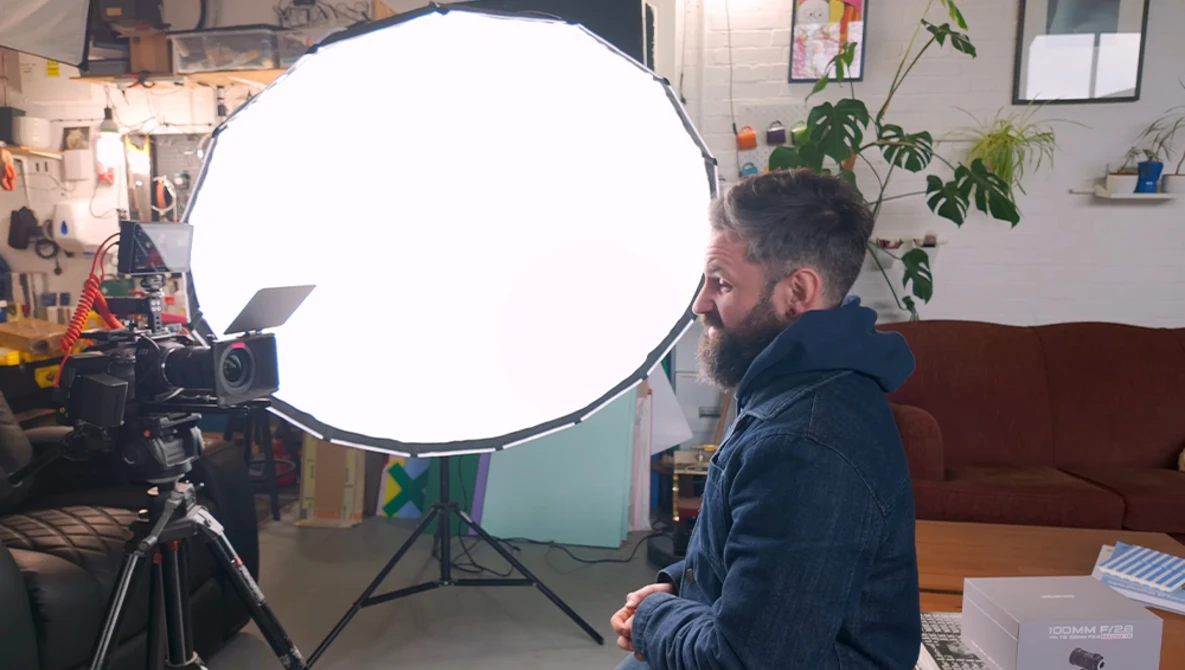 Photographer positioned beside large circular softbox reflector mounted on tripod during studio session.