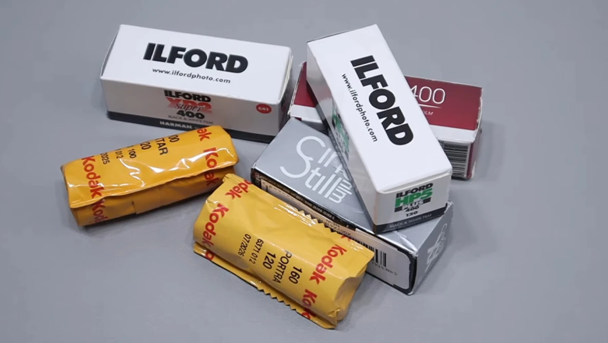 Collection of film photography stock boxes arranged on gray surface, including Ilford and Kodak brands in various speeds and formats.