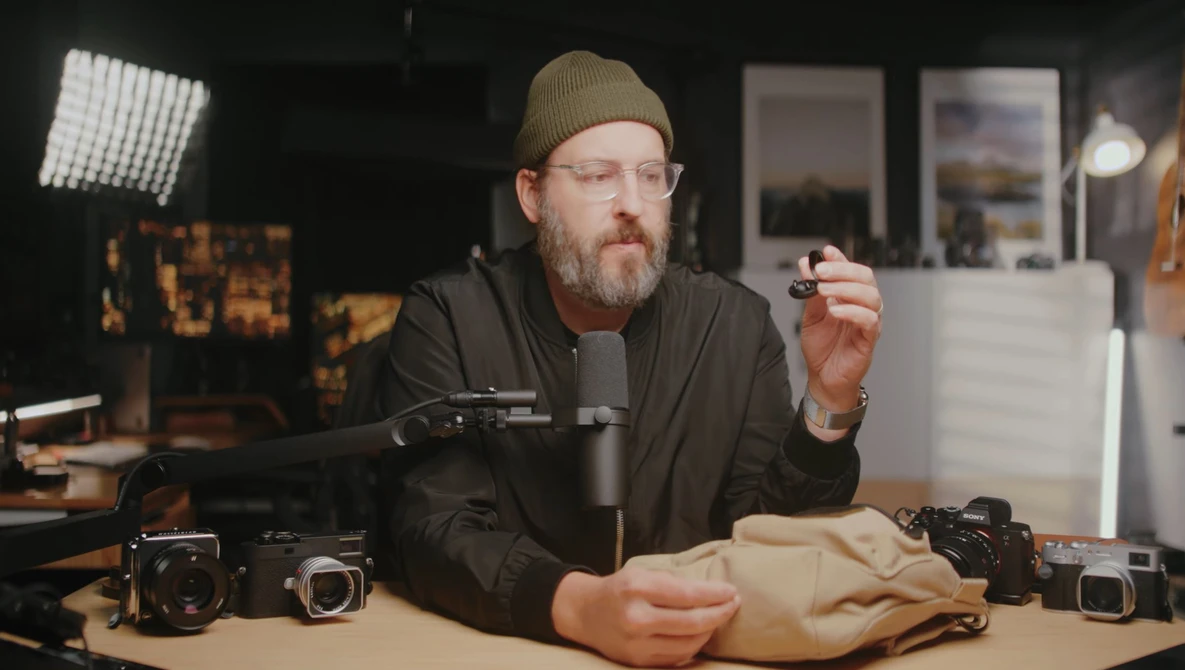 Photographer in studio holding camera gear while discussing equipment setup and techniques.