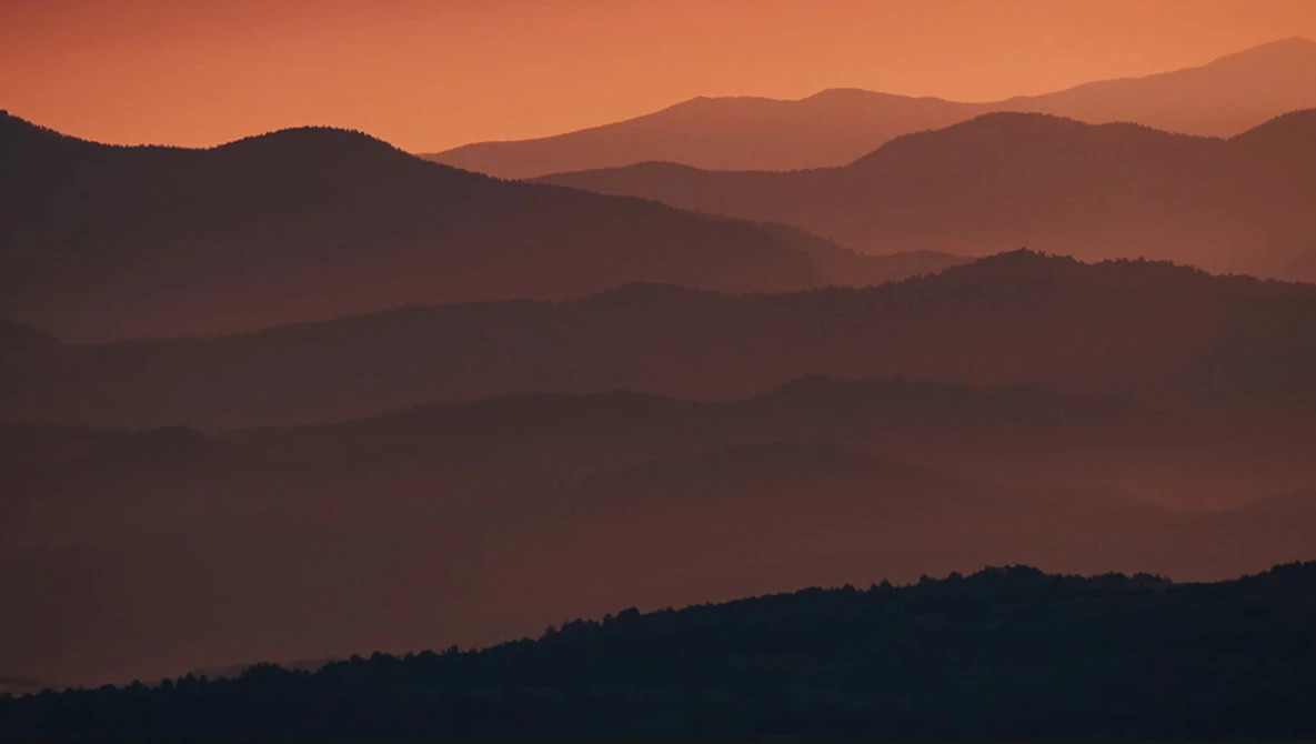 Layered mountain ridges silhouetted against an orange and amber sunset sky.