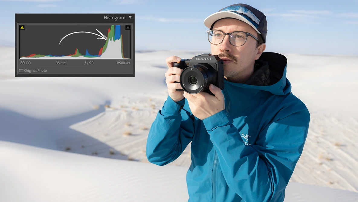 Photographer in blue jacket holding DSLR camera with histogram panel overlay displayed.
