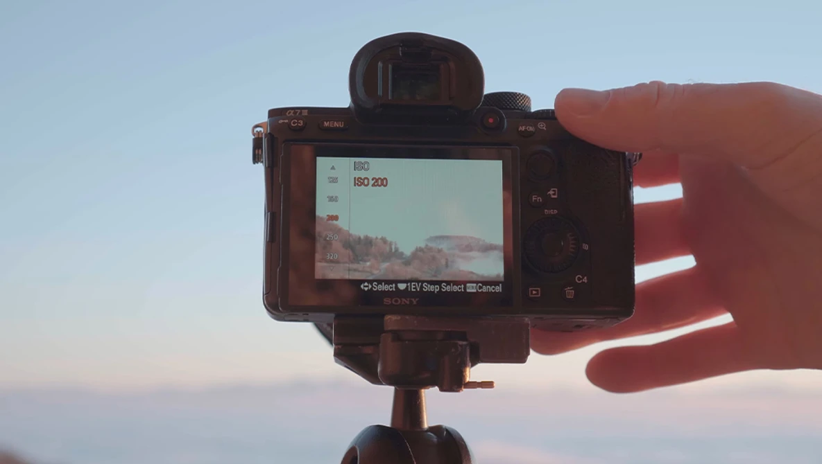 Camera mounted on tripod displaying landscape preview on rear screen during golden hour.