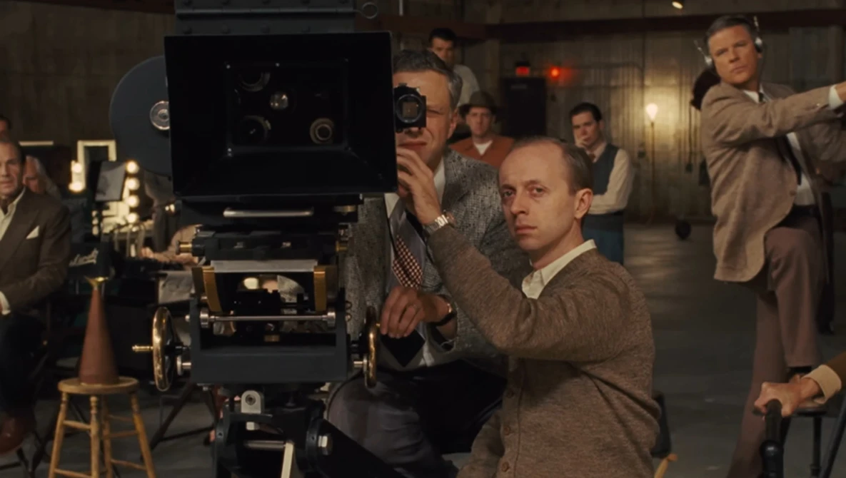 Film director operating a large format movie camera on set with crew members surrounding.
