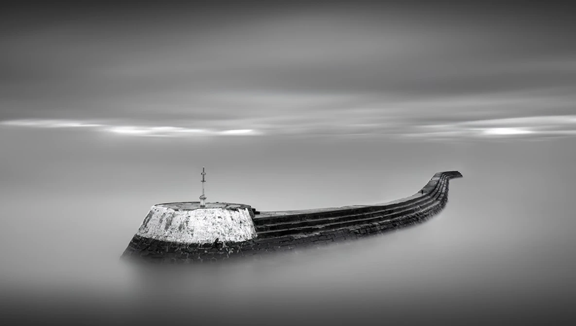 Abandoned wooden boat with snow-covered hull half-submerged in still water.