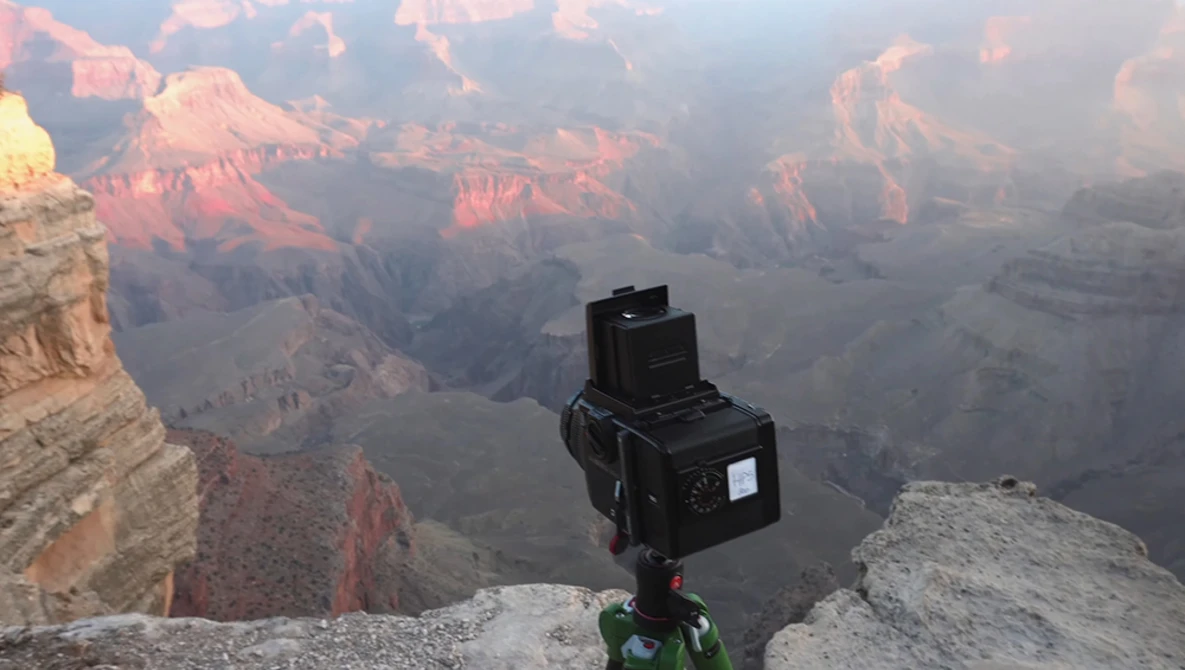 Medium format camera mounted on tripod at Grand Canyon's edge during golden hour sunrise.
