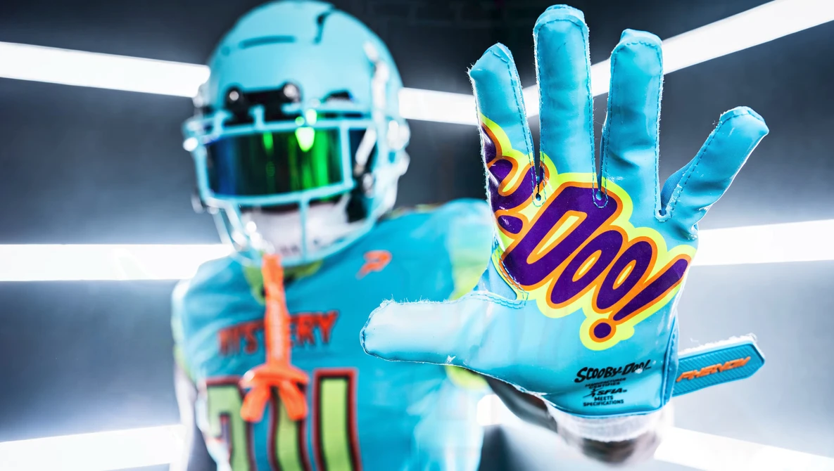 Football player in bright blue uniform extending hand toward camera, wearing colorful receiver gloves with purple and gold design.
