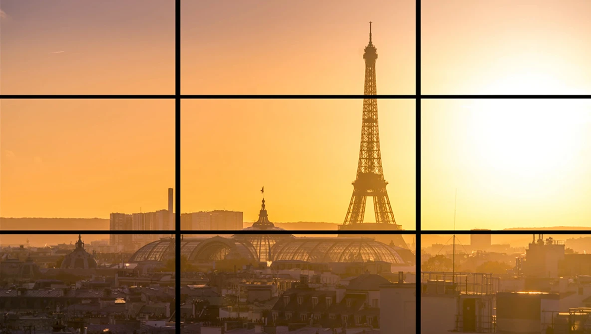 Eiffel Tower silhouetted against golden sunrise with Paris cityscape and grid window frame overlay.
