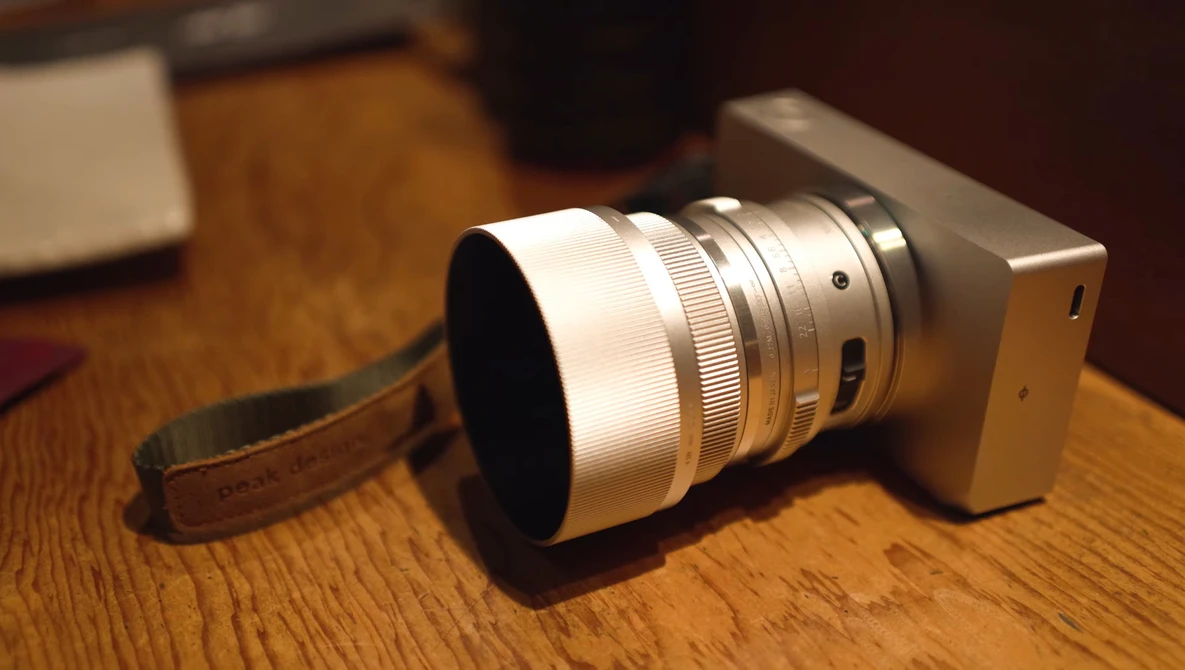 Compact camera with telephoto lens and wrist strap on wooden surface.