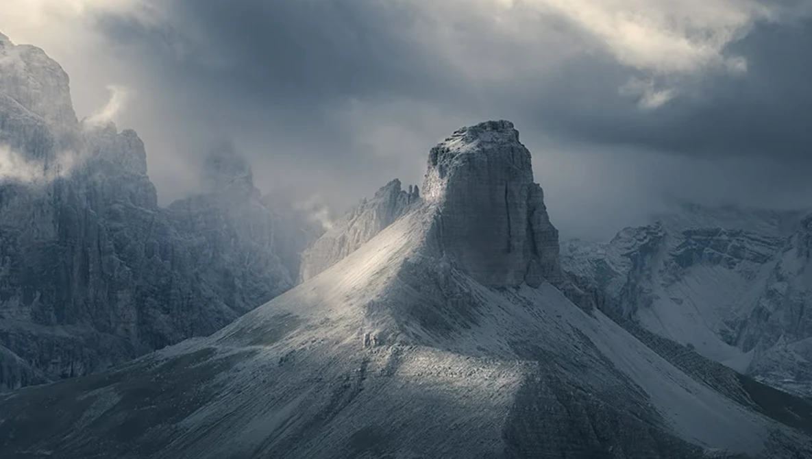 Snow-covered mountain peak rising through clouds in dramatic alpine landscape.