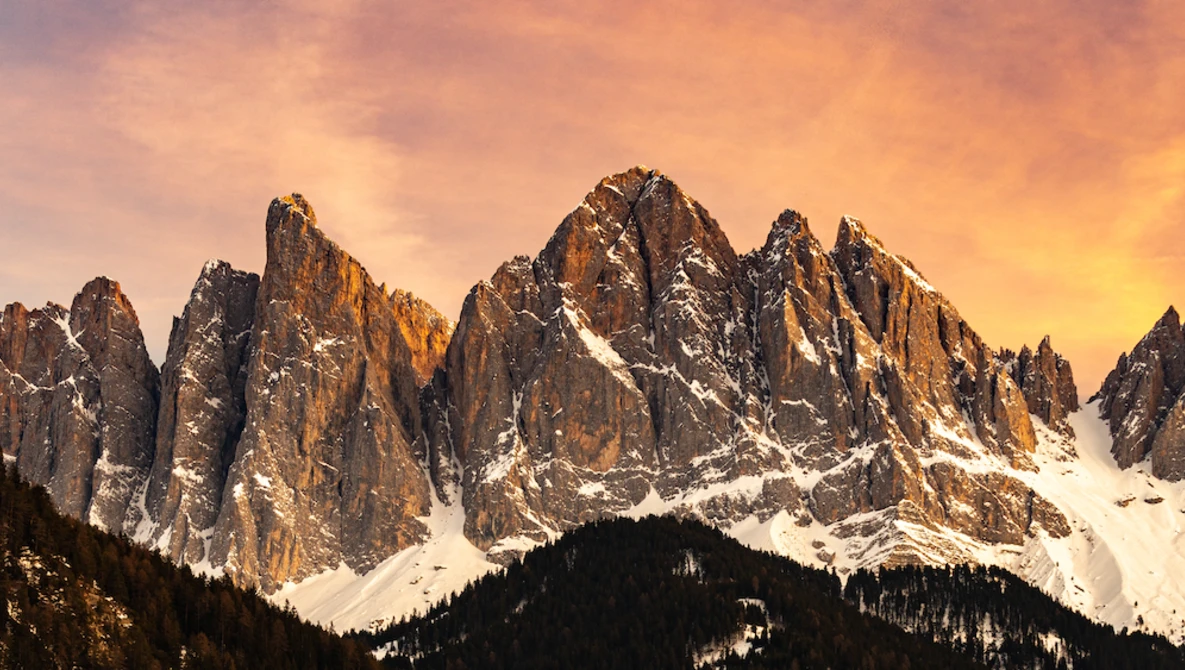 Snow-capped mountain peaks with jagged rock formations glowing in golden sunset light.