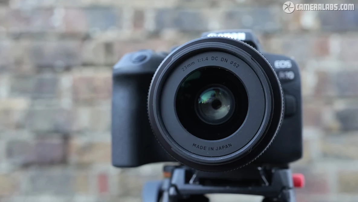 DSLR camera with wide-angle lens mounted on tripod head, shot against blurred urban brick building background.