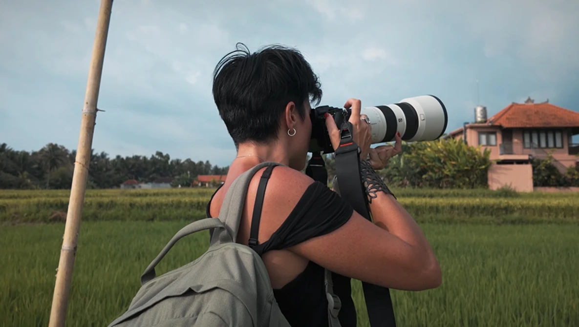 Photographer with telephoto lens shooting in rice paddy landscape with colonial building in background.